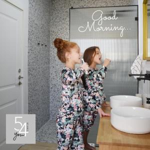 two girls in pajamas brushing their teeth in a bathroom at 54You in Ahuzat Barak