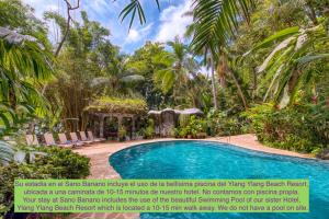 a swimming pool in a garden with palm trees at El Sano Banano Beachside Hotel in Montezuma