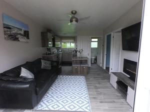 ein Wohnzimmer mit einem schwarzen Ledersofa und einer Küche in der Unterkunft JJs Lodge Holiday Home Bude in Kilkhampton