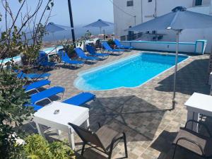 a pool with chairs and a table and an umbrella at Stella Nomikou Apartments in Firostefani