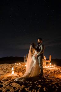 a bride and groom standing on the beach at night at Sahara Majestic Luxury Camp in Merzouga