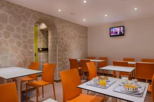 un restaurant avec des tables et des chaises ainsi qu'une télévision murale. dans l'établissement Hotel Bel Oranger Gare de Lyon, à Paris