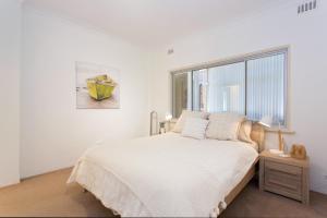 a white bedroom with a large bed and a window at Arcadia Apartment - Cottesloe in Perth