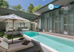 a swimming pool with an umbrella and a house at SALA Phuket Mai Khao Beach Resort in Mai Khao Beach