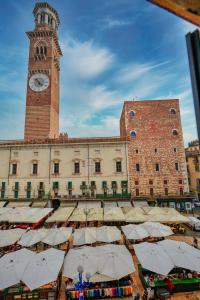 ein Gebäude mit einem Uhrturm und einem Markt mit Sonnenschirmen in der Unterkunft ApartmentsArena - Suite Mercatorum - Piazza Erbe in Verona