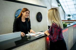 a woman standing at a counter talking to a customer at Grand Hotel Tuzla in Tuzla