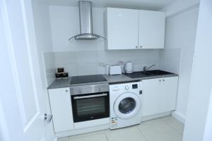eine weiße Küche mit einer Waschmaschine und einem Waschbecken in der Unterkunft Cosy Room with en-suite bathroom and shared kitchen in Thamesmead