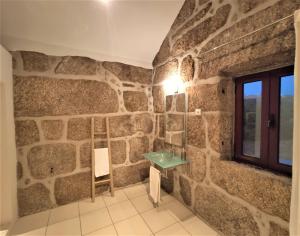 uma casa de banho com paredes de pedra, um lavatório e uma janela. em Quinta da Adarnela em Lagares da Beira