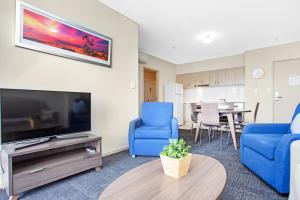 a living room with blue chairs and a flat screen tv at Hume Serviced Apartments in Adelaide