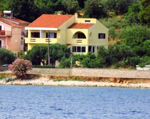 a yellow house with a red roof next to the water at Apartment by the sea and with beautiful view, 2 bedrooms, 4 persons in Kali