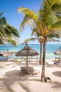 a beach with chairs and palm trees and the ocean at Le Peninsula Bay Beach Resort & Spa in Blue Bay