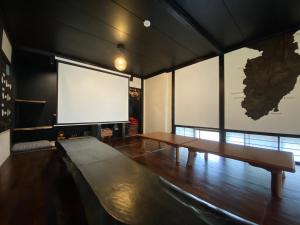 伊豆市にあるホステル ノットのテーブルと大画面テレビ付きの広い客室です。
