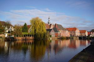 a city with a river with buildings and a church at Stadthuuske in Emden