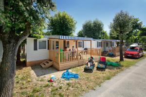 a tiny house with a family sitting on the porch at Albatross Mobile Homes on Camping Bella Italia in Peschiera del Garda
