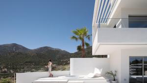 a woman walking on the balcony of a white building at Ode Iconic Residence, forever in blue - Best Villa, By ThinkVilla in Bali