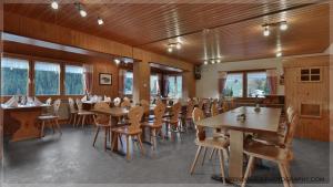 um restaurante com mesas e cadeiras de madeira e janelas em Gasthaus Bellawiese em Sankt Antönien