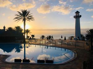 a lighthouse and a pool with a palm tree and the ocean at PHARUS retro beach home New Heated Pool in Maspalomas