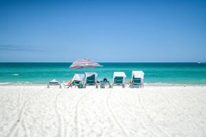Anna Maria Beach Resort في هولمز بيتش: مجموعة من الكراسي ومظلة على الشاطئ