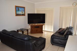 sala de estar con sofá de cuero negro y TV de pantalla plana en Christies Seahorse Holiday Townhouses, en Port Noarlunga