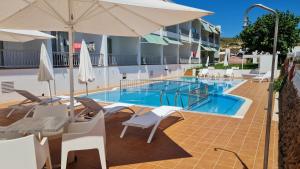 a hotel pool with chairs and an umbrella at Hostal S'Algaret in Fornells