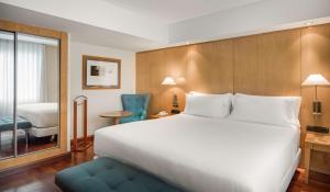 マドリードにあるNH パセオ デ ラ ハバナの大きなベッドと椅子が備わるホテルルームです。