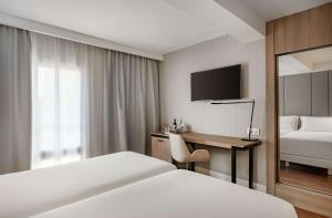 マドリードにあるNH パセオ デ ラ ハバナのベッド、デスク、テレビが備わるホテルルームです。