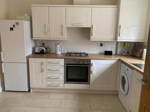 a kitchen with white cabinets and a stove and a refrigerator at Cheerful 3 bedroom home close to beach and High St in Sheringham +15 photos