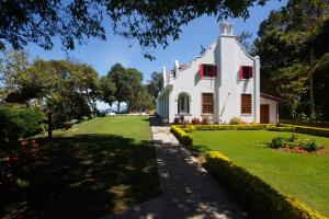 a white house with red shutters and a yard at Dutch House Bandarawela in Bandarawela