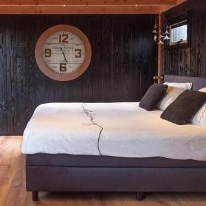 Casa aan de Plas, B&B met sauna en hottub of jacuzzi في Nieuwkoop: سرير كبير في غرفة مع ساعة على الحائط