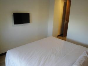 Top Hotel Manado by Gran Puri في مانادو: غرفة نوم بسرير ابيض وتلفزيون بشاشة مسطحة