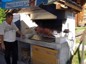 un hombre de pie junto a un horno al aire libre con una salchicha en Hotel Haus Mühlebach, en Ernen