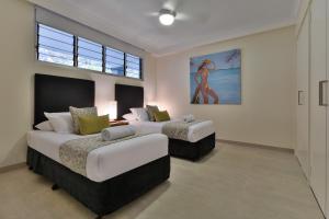 Frangipani Apartments on Hamilton Island by HIHA في جزيرة هاميلتون: غرفة نوم بسريرين ولوحة على الحائط