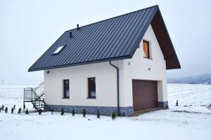 una casa blanca con techo negro en un campo nevado en Apartament CEKO, en Ostrowsko