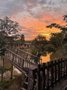 a wooden bridge over a river with a sunset at Rice straw Green lodge- resort in Quan Tom
