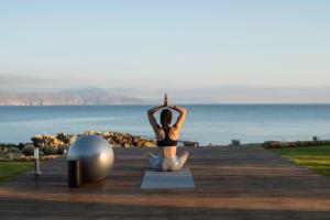 una mujer sentada en una pose de yoga en un paseo marítimo en An intimate Villa Resort- Right on the beach, by ThinkVilla, en Petres