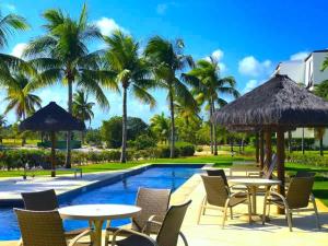 uma piscina de resort com mesas, cadeiras e palmeiras em Condominio Iberostate na Praia do Forte