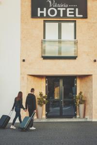 a man and woman walking past a hotel with their luggage at Hotel Viktória in Sárvár