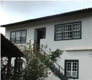 a white house with black windows and a tree at Quartos Sierra Tiradentes in Tiradentes