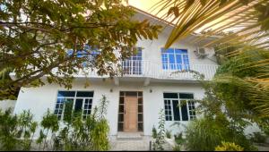 a white house with blue windows and trees at Dhonveli Inn, Bandidhoo in Meedhoo