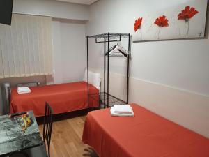 Habitación con 2 camas con sábanas rojas y mesa. en Pensión El Espolón en Logroño