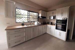 eine Küche mit weißen Schränken, einem Waschbecken und einem Fenster in der Unterkunft Mango Vert House in Arima