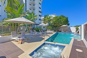 a swimming pool with chairs and an umbrella next to a building at Coco Mooloolaba in Mooloolaba