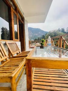 balkon z 2 drewnianymi ławkami i szklanym stołem w obiekcie The Mad King's House & Cafe w mieście Manāli