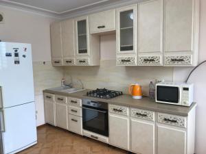 eine Küche mit weißen Schränken, einem Herd und einer Mikrowelle in der Unterkunft 1 комнатная квартира в самом центре города на Жарбосынова 71 in Atyrau