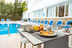 a table with a plate of food and drinks on it next to a pool at BLUESEA Piscis - Adults Only in Port d'Alcudia