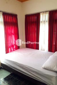 um quarto com cortinas vermelhas e uma cama com lençóis brancos em Gebby Homestay Bromo RedPartner em Pasuruan