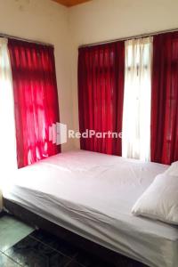 a bedroom with red curtains and a bed with white sheets at Gebby Homestay Bromo RedPartner in Pasuruan