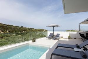 a house with a swimming pool with chairs and an umbrella at Blue Aura Villa, elegance & calm living, By ThinkVilla in Magnisía