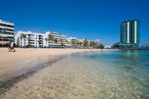 una spiaggia sabbiosa con edifici sullo sfondo e l'oceano di Apartamento Almirante VV ad Arrecife