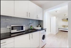 uma cozinha com armários brancos e uma máquina de lavar e secar roupa em New Spacious 1 bed studio flat in Aldgate em Londres